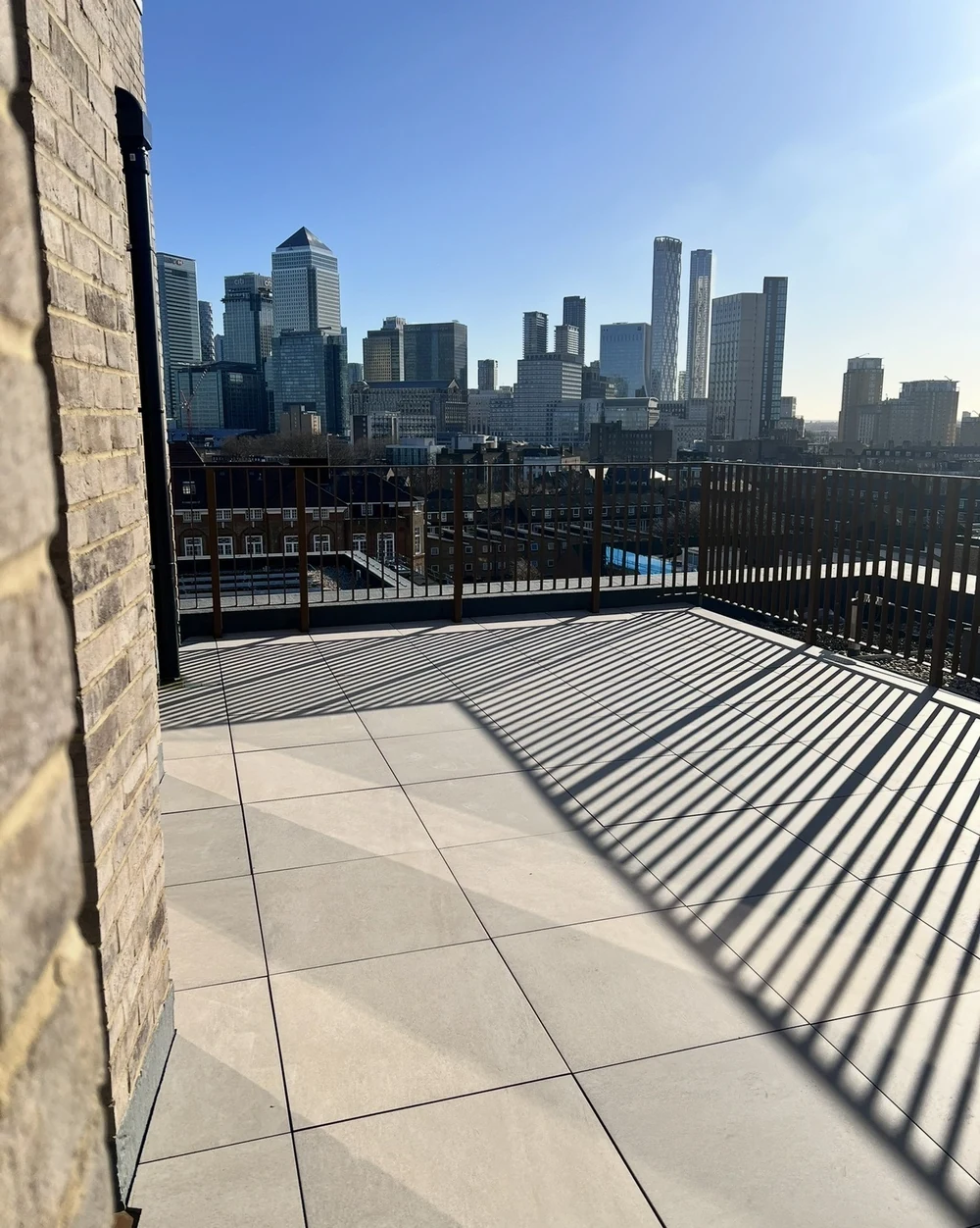 Paved roof terrace with long shadows and a view across the city skyline